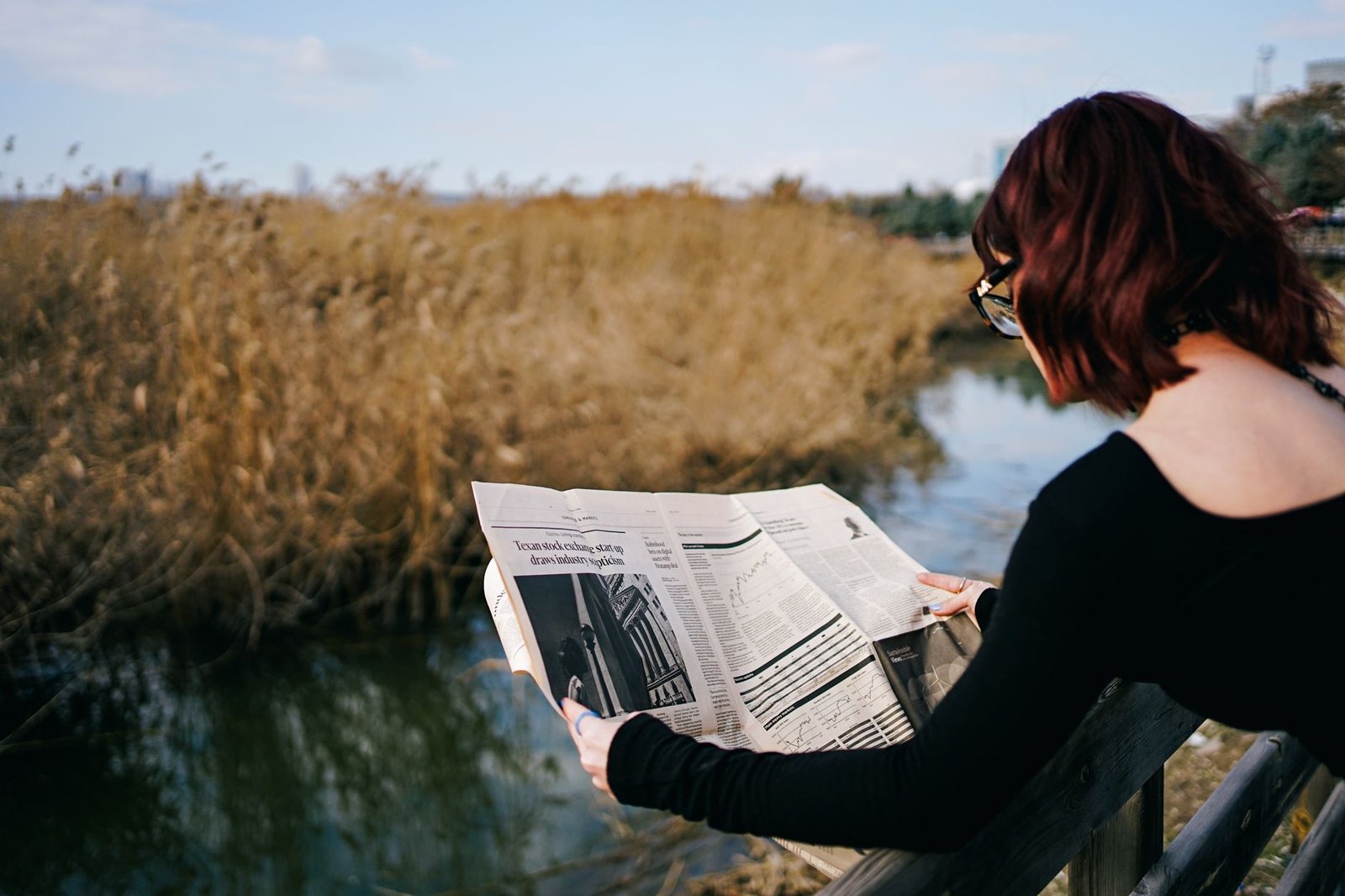 A woman reads a newspaper by a river, surrounded by autumn reeds and tranquil scenery. — Best Non GamStop Casino UK Reviews a