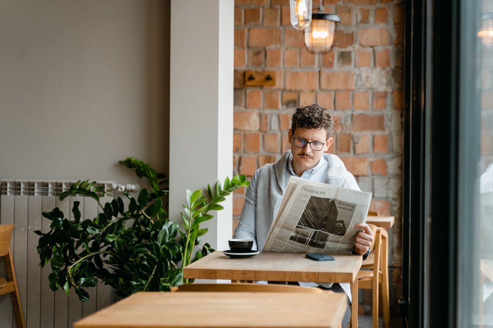 A man with glasses enjoys coffee and reads a newspaper in a cozy café setting. — Best Non GamStop Casino UK Reviews and Ranki