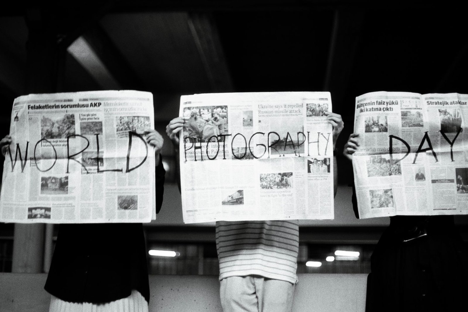 Three people hold newspapers with 'World Photography Day' text, artistic vibe. — Best Non GamStop Casino UK Reviews and Ranki