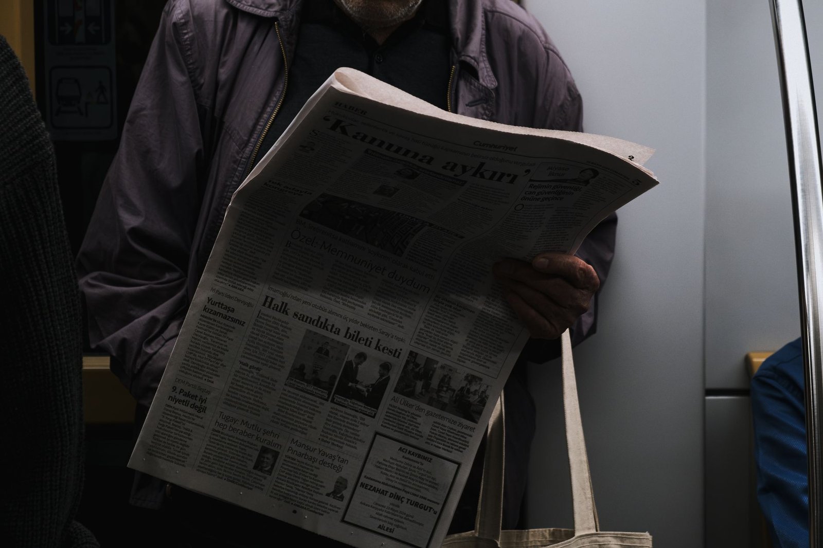 A man reads a newspaper in a dimly lit public transport setting, reflecting city life. — Desata el Poder de Zeus y Multiplica