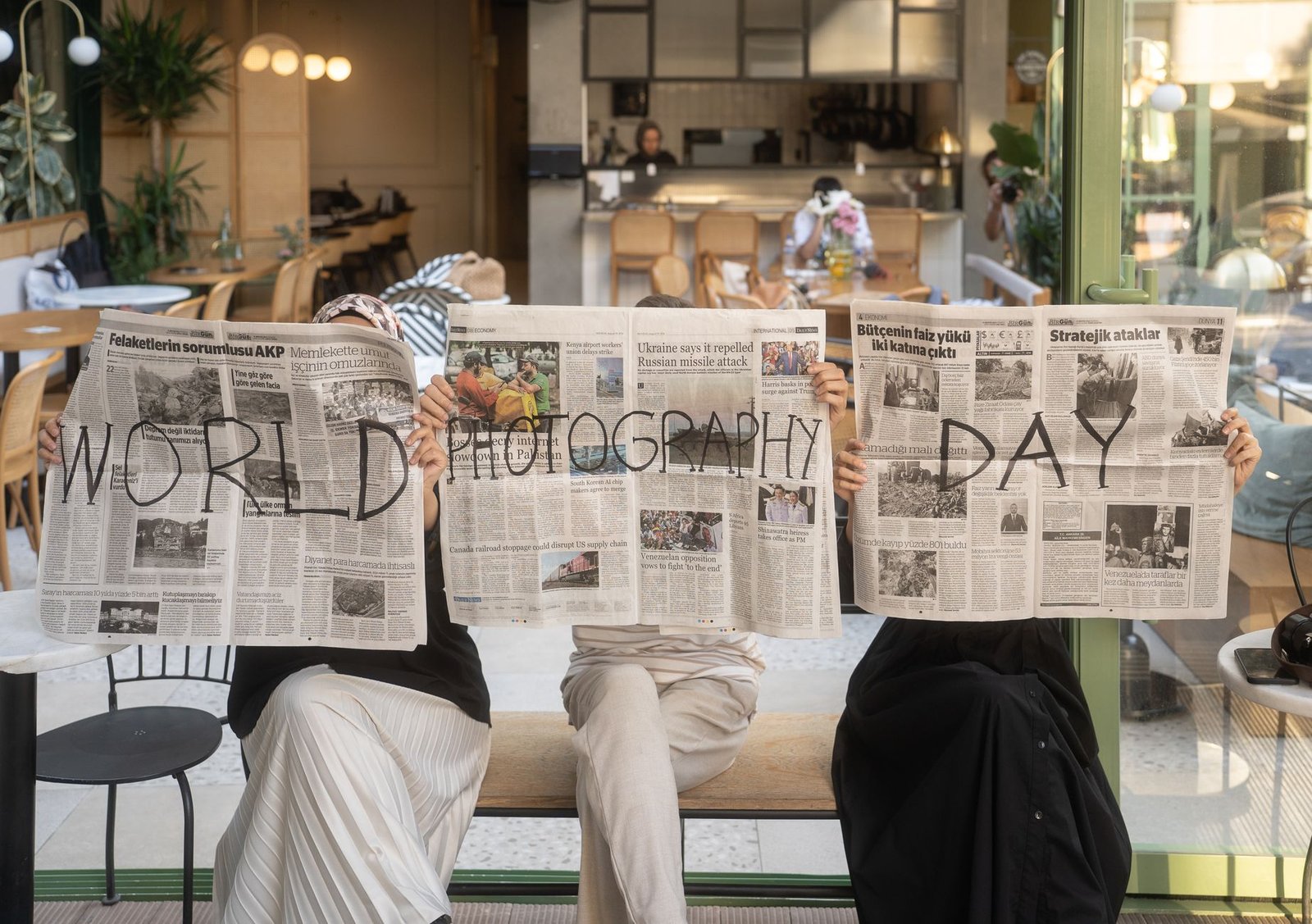 Three people holding newspapers promoting World Photography Day in a cozy Ankara café. — Finest On-line Casinos Uk: Prime On