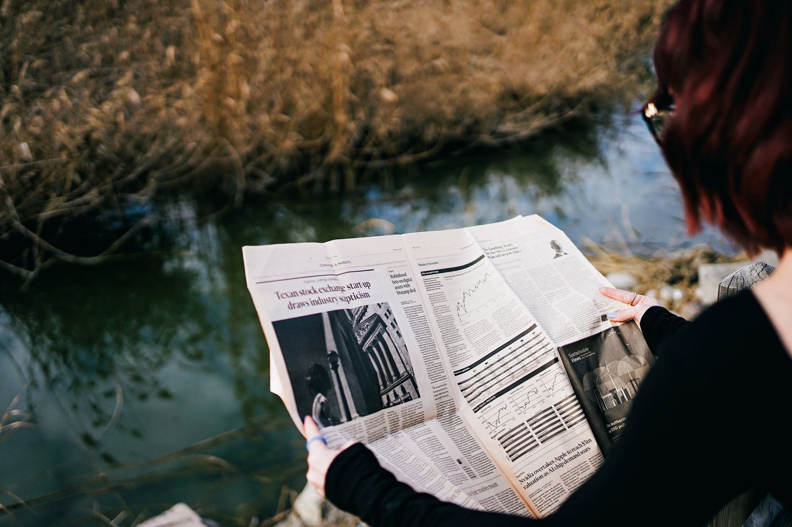 A woman reads a newspaper by a river surrounded by autumn foliage. — Fraga Casino yeni oyunular n bldi.2237
