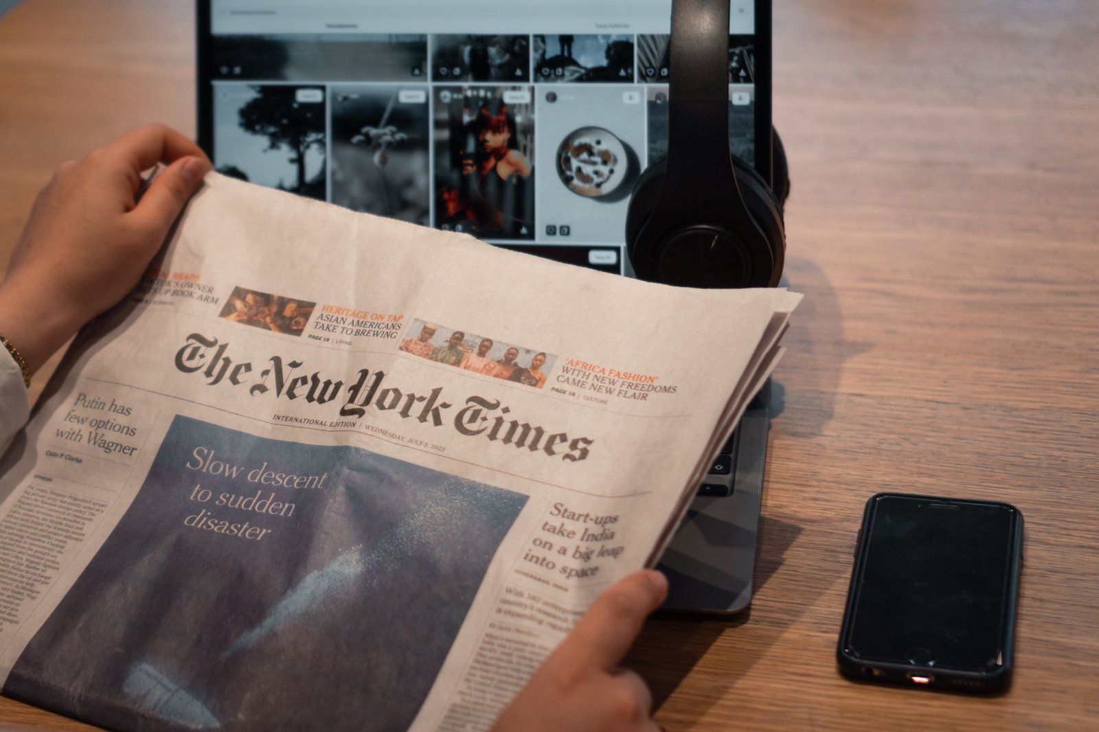 Close-up of hands holding a newspaper by a laptop and smartphone on a table. — How The Online On Line Casino Business Is Perf