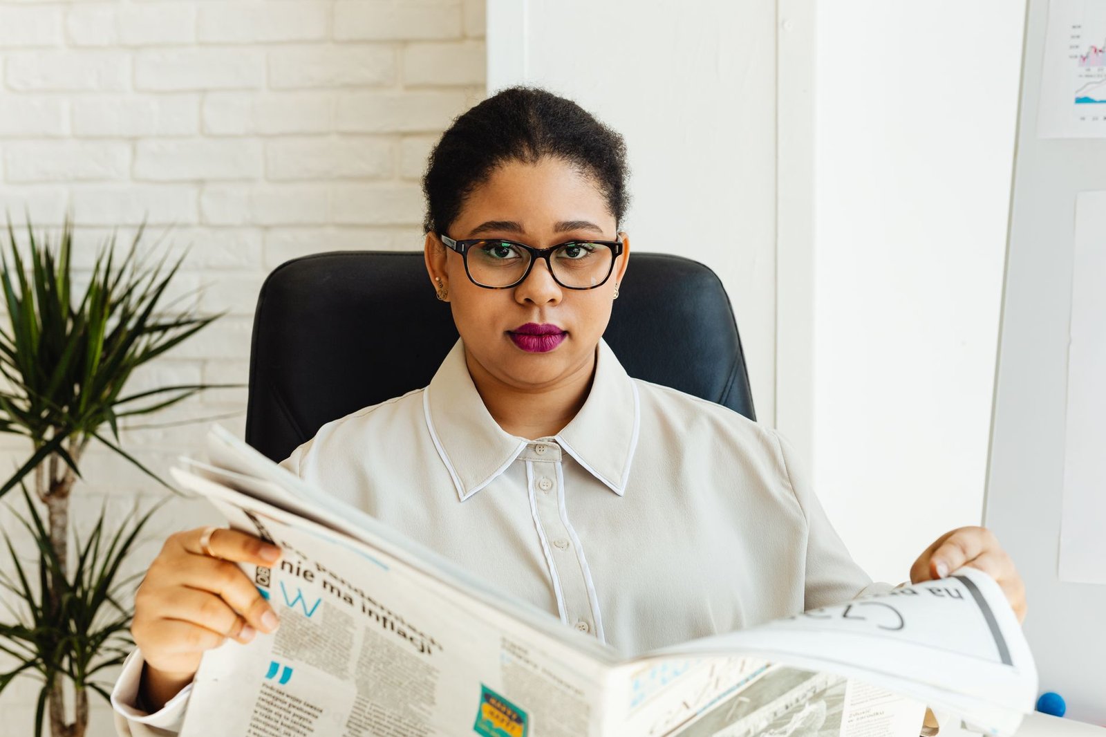 Professional woman with glasses reading a newspaper at her office desk, surrounded by modern decor. — Magyar Online Casino a