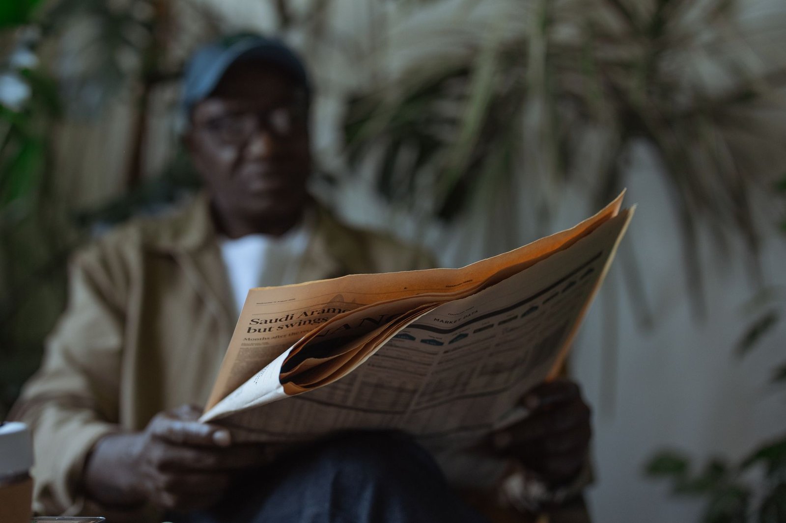 An adult man reading a newspaper indoors, surrounded by plants with a blurred background. — Online Pokies